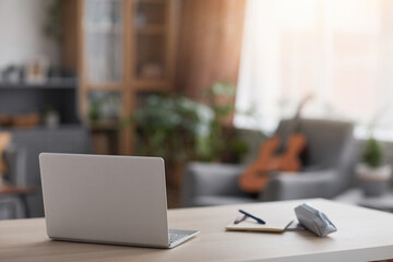 Minimal image of laptop computer on desk in teenage boys room, blurred guitar in background, copy...