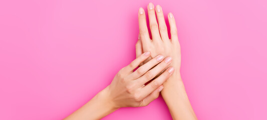 Obraz na płótnie Canvas top view of female hands with pastel nail polish on nails on pink background, banner