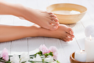 Obraz na płótnie Canvas groomed female feet near bowl on wooden surface near eustoma flowers and candles on blurred foreground