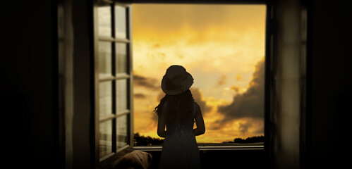 a girl in indoor home window looking outside at sunset evening.