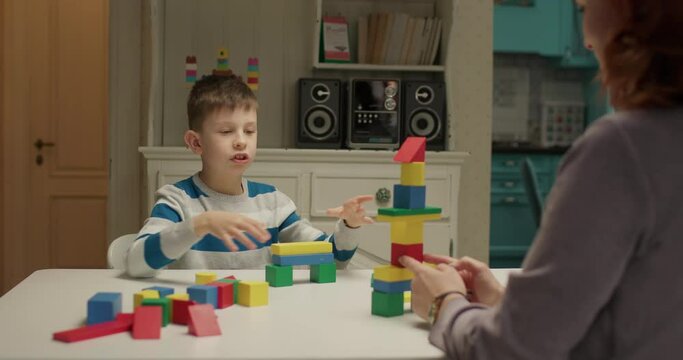 Autism teacher working with kid with autism with wooden blocks. Boy with autism learning with therapist at home. Child building with wood blocks. Autism spectrum disorder education.