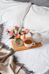 Obraz na płótnie Canvas Tray of tea on bed. White bedding sheets with blanket and pillow. Breakfast in bed. Warm and cosy scandinavian hygge concept - cup of tea.