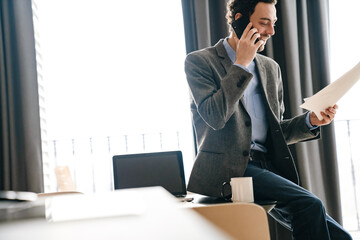 Smiling businessman talking on mobile phone while examining documents