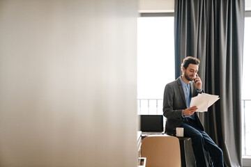 Pleased businessman talking on mobile phone while examining documents