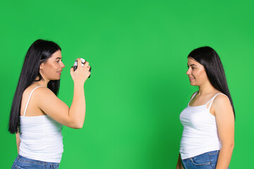 The sisters pose and take pictures with a vintage camera. Green background with empty space.