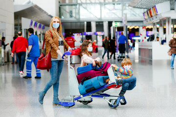 Two little kids, boy and girl and mother in medical mask at airport. Children, family travel by plane during corona virus pandemic lockdown. People in mask as preventive measure and covid protection - obrazy, fototapety, plakaty