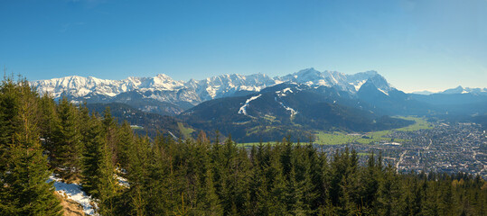 view from Wallberg mountain over fir trees to Garmisch-Partenkirchen tourist resort and Zugspitze mountain mass