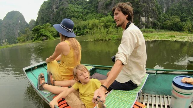 A young family on a boat having a river trip among spectacular limestone rocks in Ninh Binh, a tourist destination in northern Vietnam. Travel to Vietnam concept