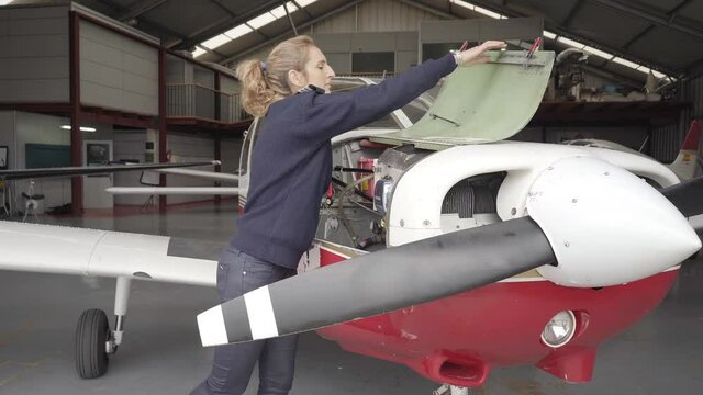 Pilot woman in the hangar doing the maintenance of the engine of a small plane. Pre-flight preparations.