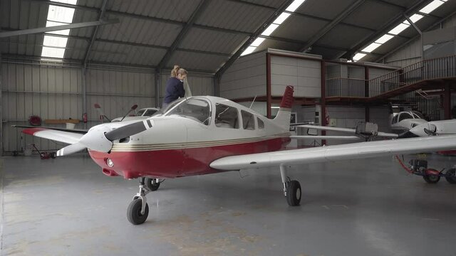 Young female pilot discovering light aircraft with protective cover in hangar.
