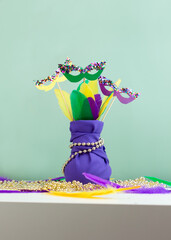 Mardi Gras decoration. Bouquet of multicolored feathers and masks in violet cloth vase. Party invitation. Shrove Tuesday, Fat Tuesday