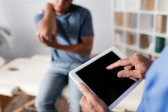 cropped view of doctor pointing with finger at digital tablet near african american patient on blurred background