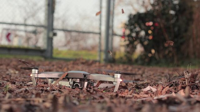Drone taking off in fallen leaves, wind from rotor blowing autumn leaves in the air in spectacular mess. Slow motion from 120 fps