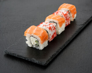 california sushi with red tobiko caviar and slices of philadelphia sushi on black slate board