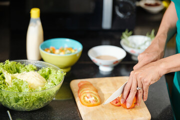Close-up image of housewife cutting fresh tomatoes with sharp knofe when making salad at kitchen counter