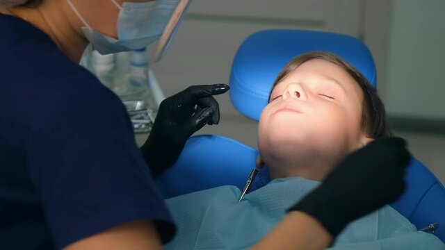 Dentist rinses boy's mouth water holding saliva ejector during oral hygienic cleaning, face closeup. Visit hygienist in stomatology clinic, brushing teeth. Teeth cure and treatment concept.