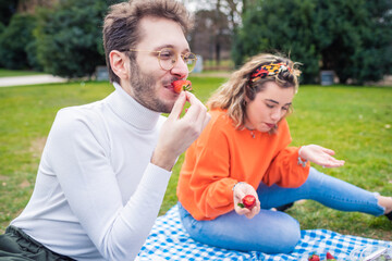 Two caucasian friends having picnic in a park eating strawberries