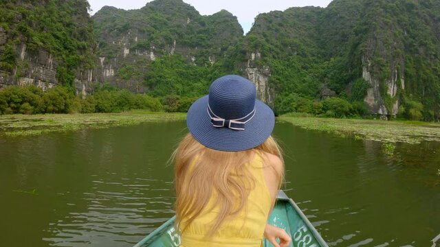 A young woman on a boat having a river trip among spectacular limestone rocks in Ninh Binh, a tourist destination in northern Vietnam. Travel to Vietnam concept