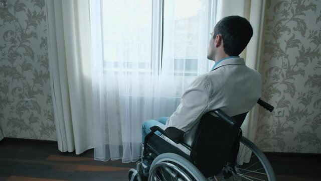 Disabled man in a wheelchair looks through the window