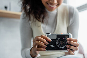 cropped view of smiling african american woman holding vintage photo camera, blurred background