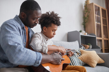 Modern African American man spending free time with his teen son at home teaching him how to play...