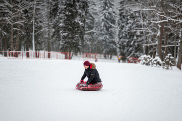 Fototapeta na wymiar Active winter leisure. Tubing. A teenage boy rolls down a hillside in the woods on a tube.