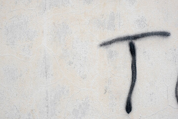 White painted aged, grunge wall texture with the letter T in spray paint , background. Stock Photo.