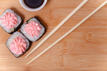 Sushi maki rolls with chopsticks on bamboo table with soy sauce, top view