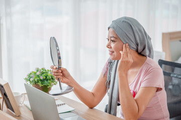 Young asian women wearing hijab Look in the mirror at your desk Represents recovery from a breast cancer illness. breast cancer concept, cancer prevention concept.