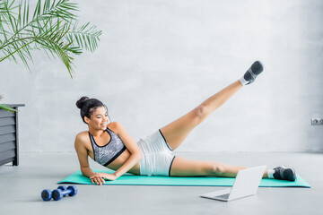 young african american woman in sportswear exercising on fitness mat near laptop at home © LIGHTFIELD STUDIOS