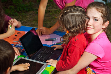 Children learn to draw on colored pieces of paper. Laptop, pencils and markers on a blue table. Boys and girls play in nature.