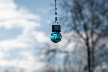 Piękna szklana niebieska lampka solarna ogrodowa, wyizolowana z tła, wisząca w ogrodzie