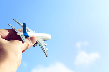 close up photo of man's hand holding toy airplane against blue sky with clouds