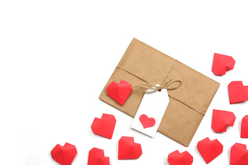Gift wrapped in brown craft paper, tied with twine with a bow, with label with heart, surrounded by several handmade red 3D paper hearts on white background isolated copy space