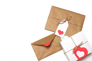 White gift box with red label in a heart form, gift wrapped in brown craft paper, tied with twine with a bow, envelope from craft paper with red heart on white background isolated