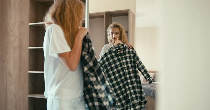 Reflection in the mirror of the young attractive woman with blonde curly hair trying on the green dress on the hander.