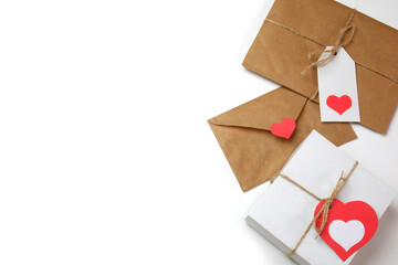 White gift box with red label in a heart form, gift wrapped in brown craft paper, tied with twine with a bow, envelope from craft paper with red heart on white background isolated