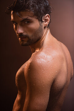 sexy, wet, muscular man looking at camera on dark background