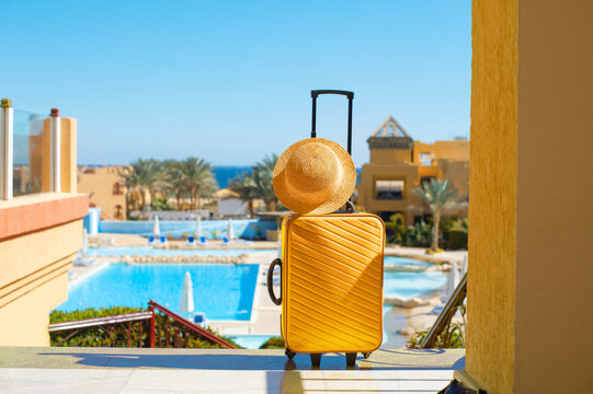 Travel, summer holidays and vacation concept yellow suitcase with hat on background of hotel pool area in Egypt