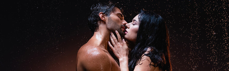 side view of sexy brunette woman and shirtless man kissing with closed eyes on dark background...