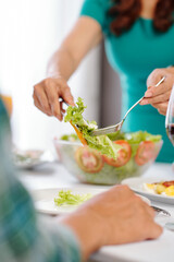 Obraz na płótnie Canvas Housewife using tongs and fork when serving healthy vegetable salad for her guests at home