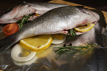 Fresh dorado fish. Stuffing fish with lemon, rosemary and other ingredients. On the foil, a wooden table and a wooden Board.
