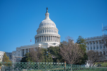 The United States Capitol Building, preparing construction for inauguration next to the fence on blue sky background.
