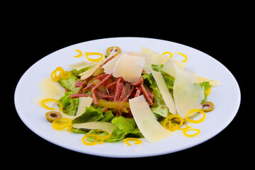 Salad with cervelat sausage, olives, lettuce, bell pepper, parmesan shavings-on a white plate on black background