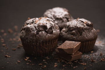 Close-up of homemade chocolate muffin on a dark background on which falls sugar.
