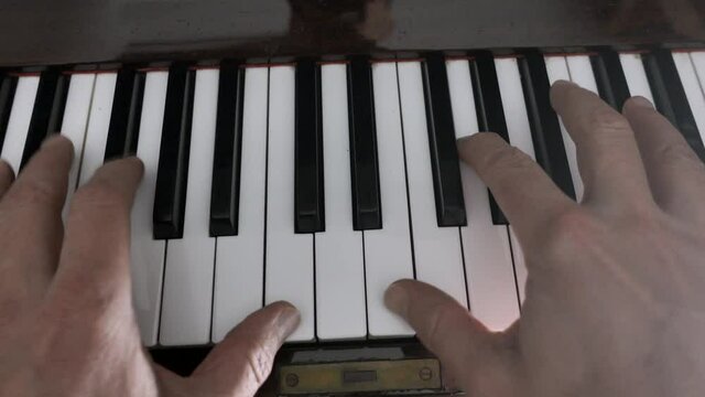 Piano being played by two hands. Close up shot of fingers playing the black and white keys of a piano
