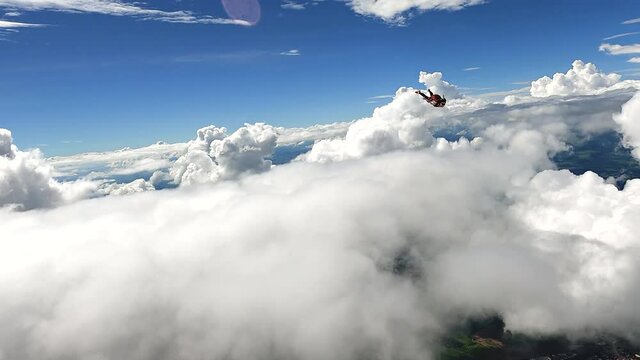 Image of a woman parachutist in casual clothes doing a dive among the clouds, in slow motion with 4K resolution.