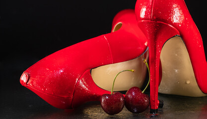 wet with water drops female shiny red stilettos and cherry berry on a black background