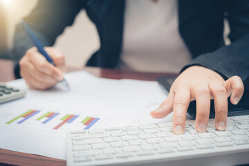 business woman hand using keyboard and typing computer technology for analysis and budget financial accounting with use pen pointing on growth statistics chart and graph on paper work.