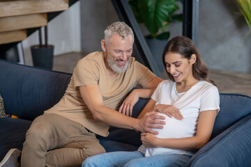 Happy mature man and young pregnant woman sitting and talking